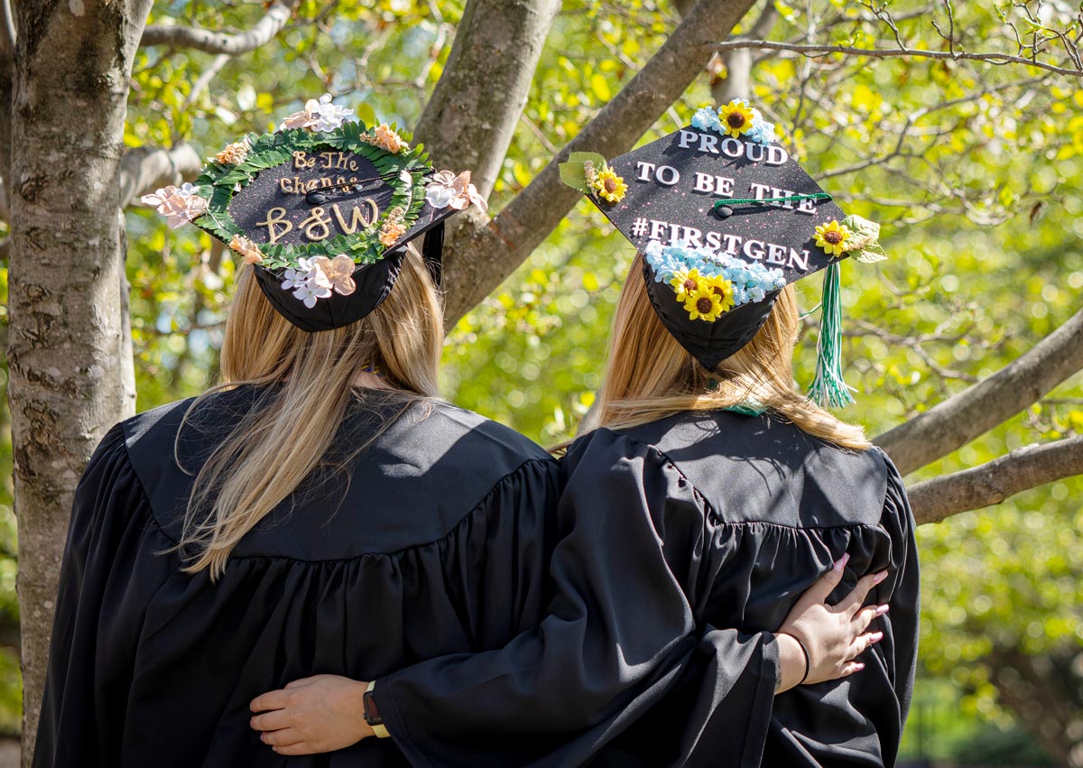 Two students embracing showing their decorated graduation caps