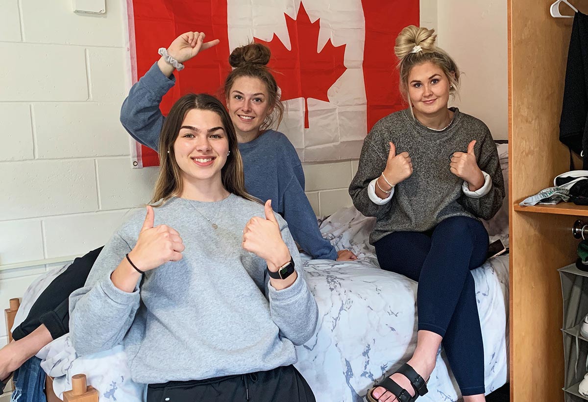 Canadian exchange students giving the camera a thumbs up in front of a Canadian flag in their dorm room