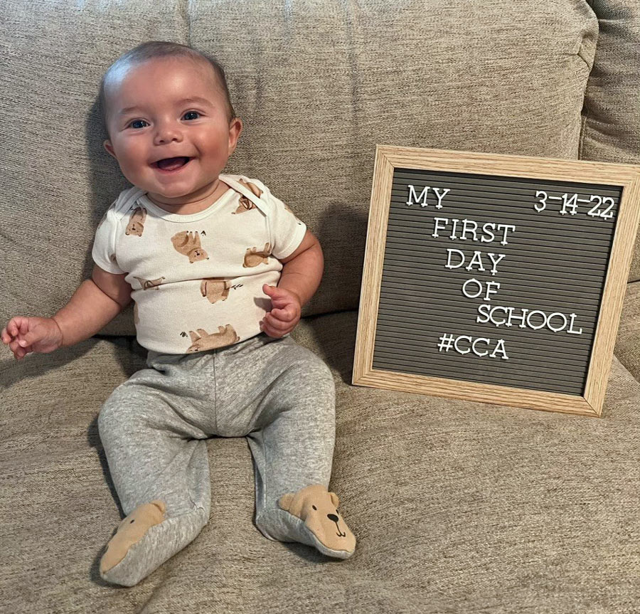 Baby Johnny Fowler sitting on  a couch with a sign that reads "My first day of school #CCA""