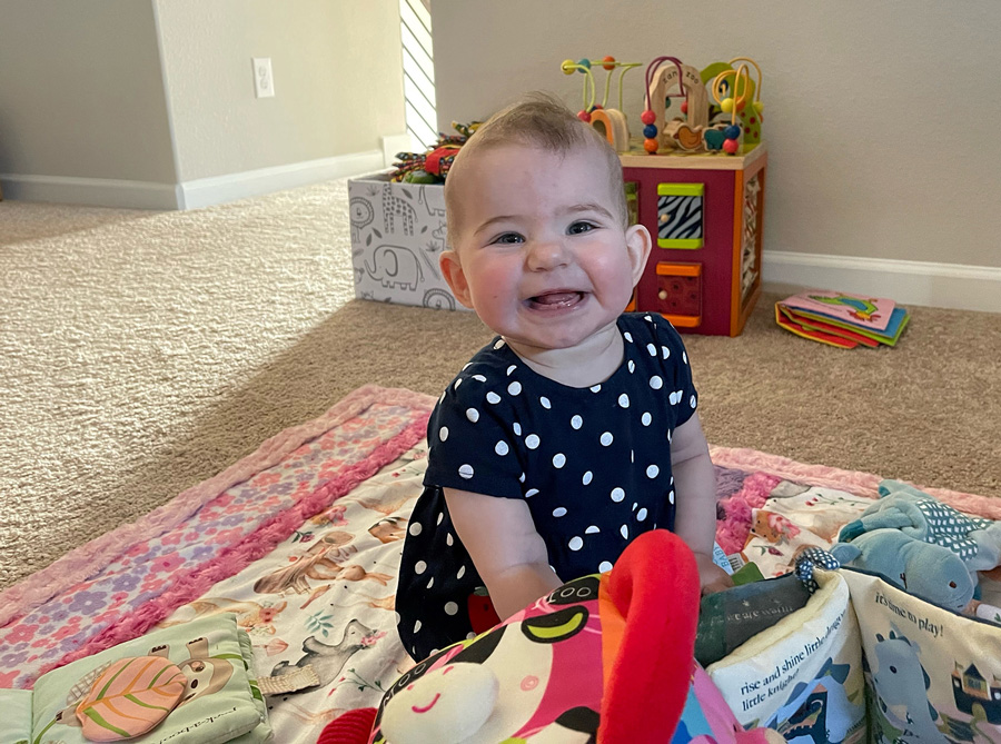Baby Paige Riley Quint smiling on a rug with toys