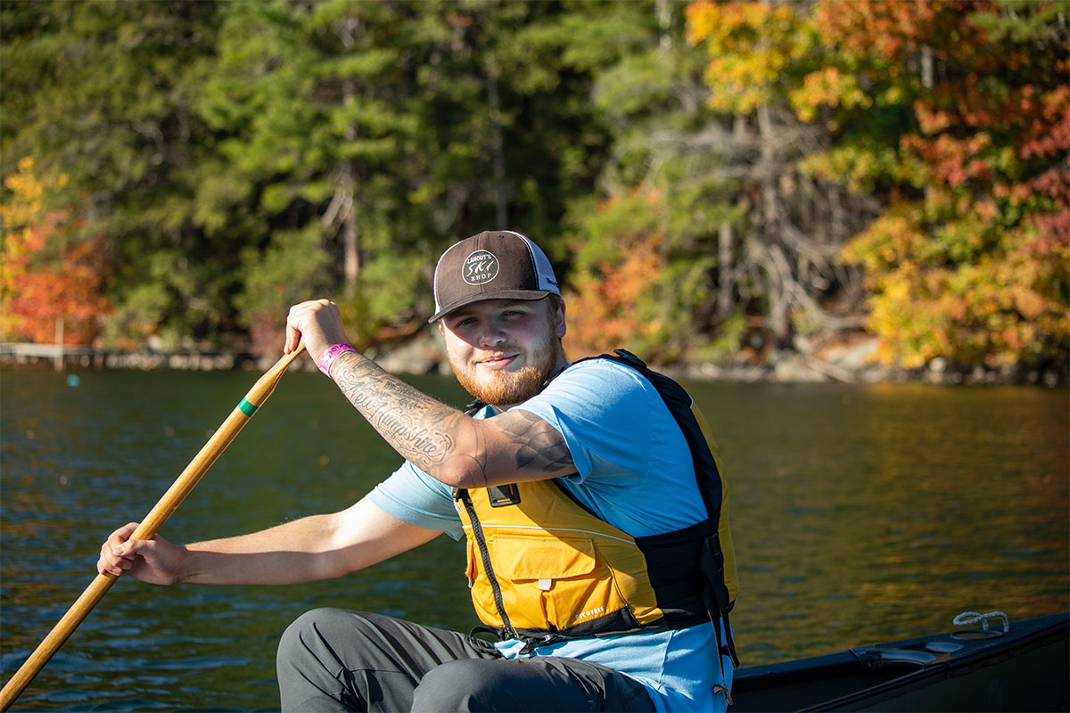 Smiling student canoeing on lake with forest in background