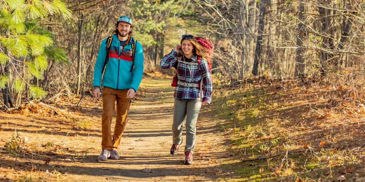 2 students with packs hiking together on a wooded trail