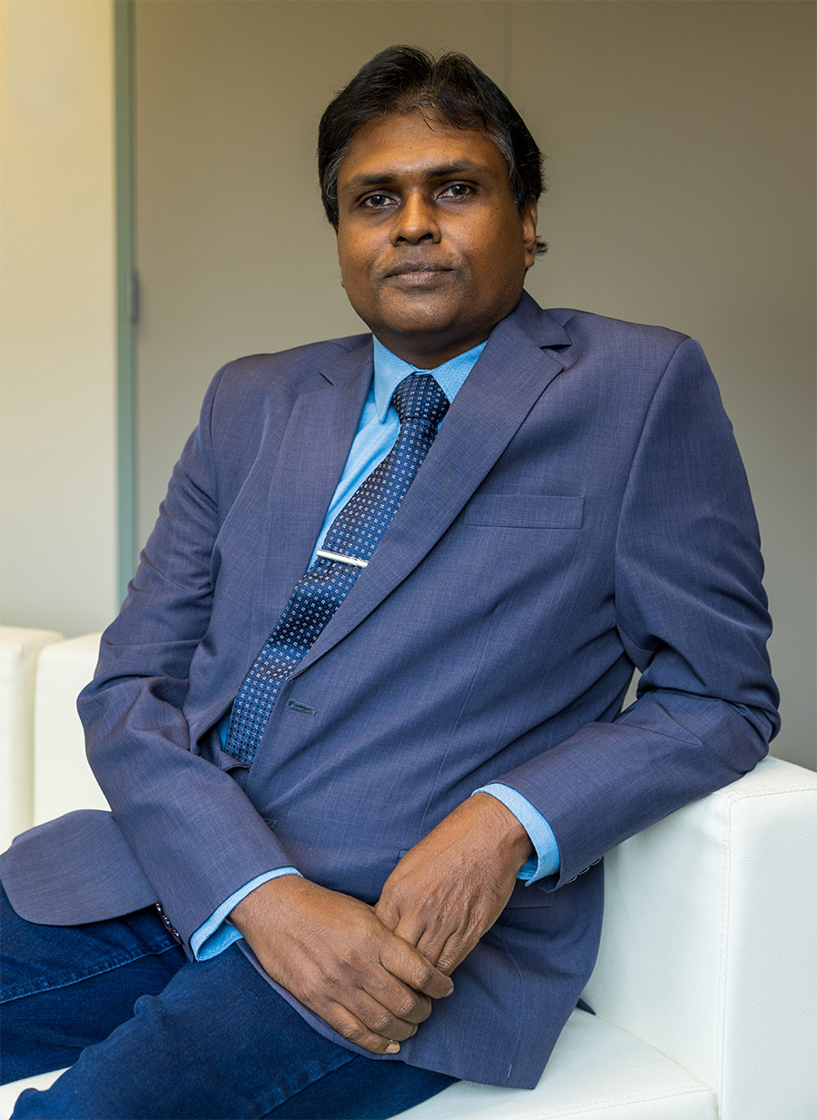 Harsha Abeykoon in suit leaning on white couch
