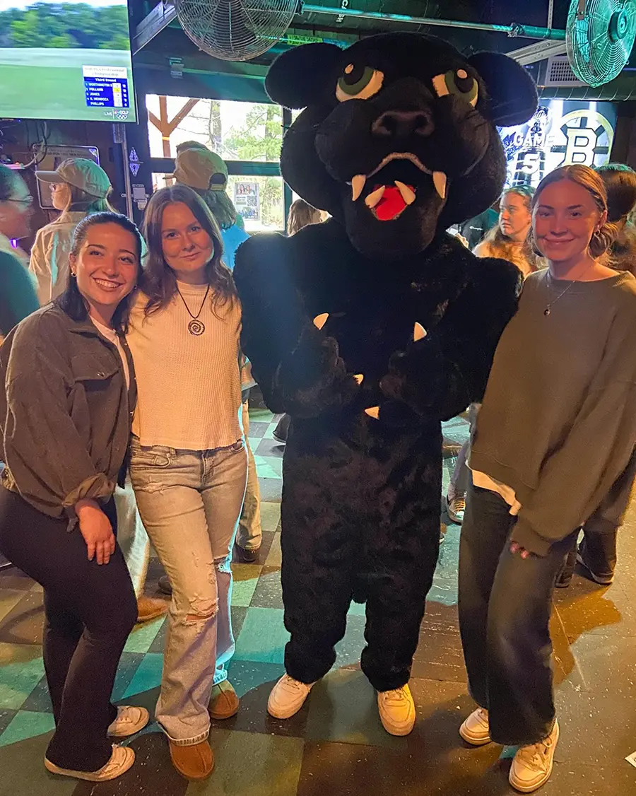 three female PSU students take a photo with Pemi the Panther at the Lucky Dog Tavern during the Pints with PSU event